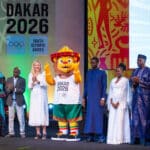 The Ayo mascot of the Dakar 2026 Youth Olympic Games on stage at its unveiling ceremony in Senegal, flanked by officials