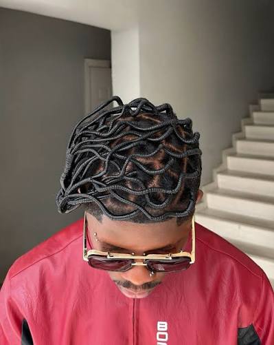 The Art of African Braiding, Through the Eyes of Gen Z 5 Emeka Onyeziri looking down, showing a woven lattice of threaded hair above his cornrows.