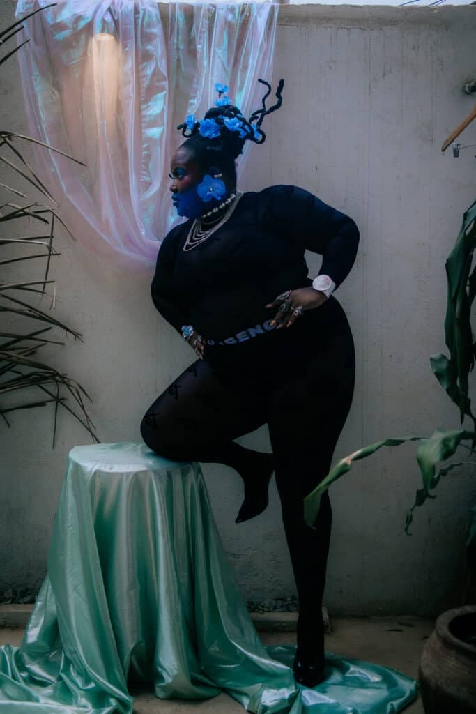 Portrait lit in blue, the subject's face painted and flowers set in the hair against an iridescent backdrop