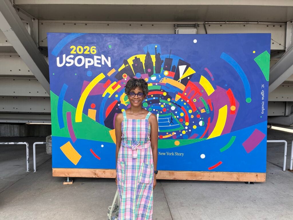 The author, TaNeesha Johnson, in front of the colourful 2026 US Open mural by Eugenia Mello at Flushing Meadows.