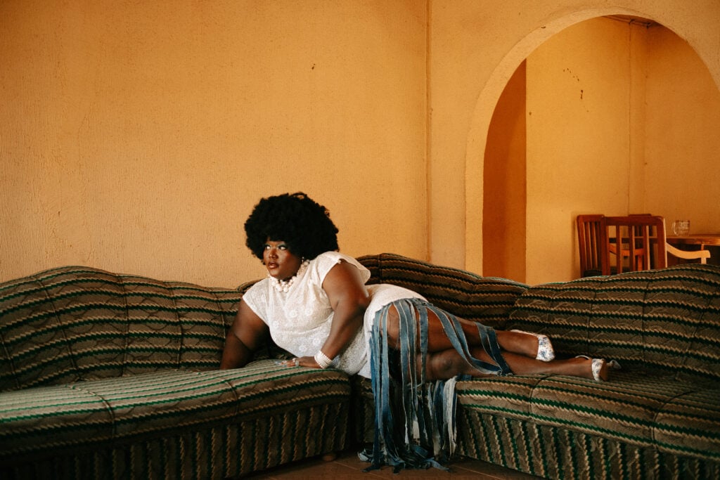 Woman with an afro reclining on a striped patterned sofa in a warm-lit room