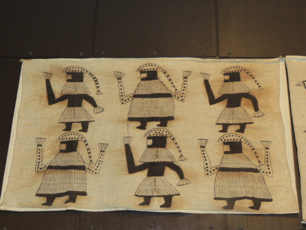 From Korhogo Cloth to Digital Print: Alia Baré and the Language of Senufo Textiles 2 Korhogo cloth with six painted figures in dark brown on undyed cotton, mounted on a dark wooden wall.