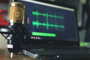 Gold-coloured studio microphone beside a laptop displaying green audio waveforms.