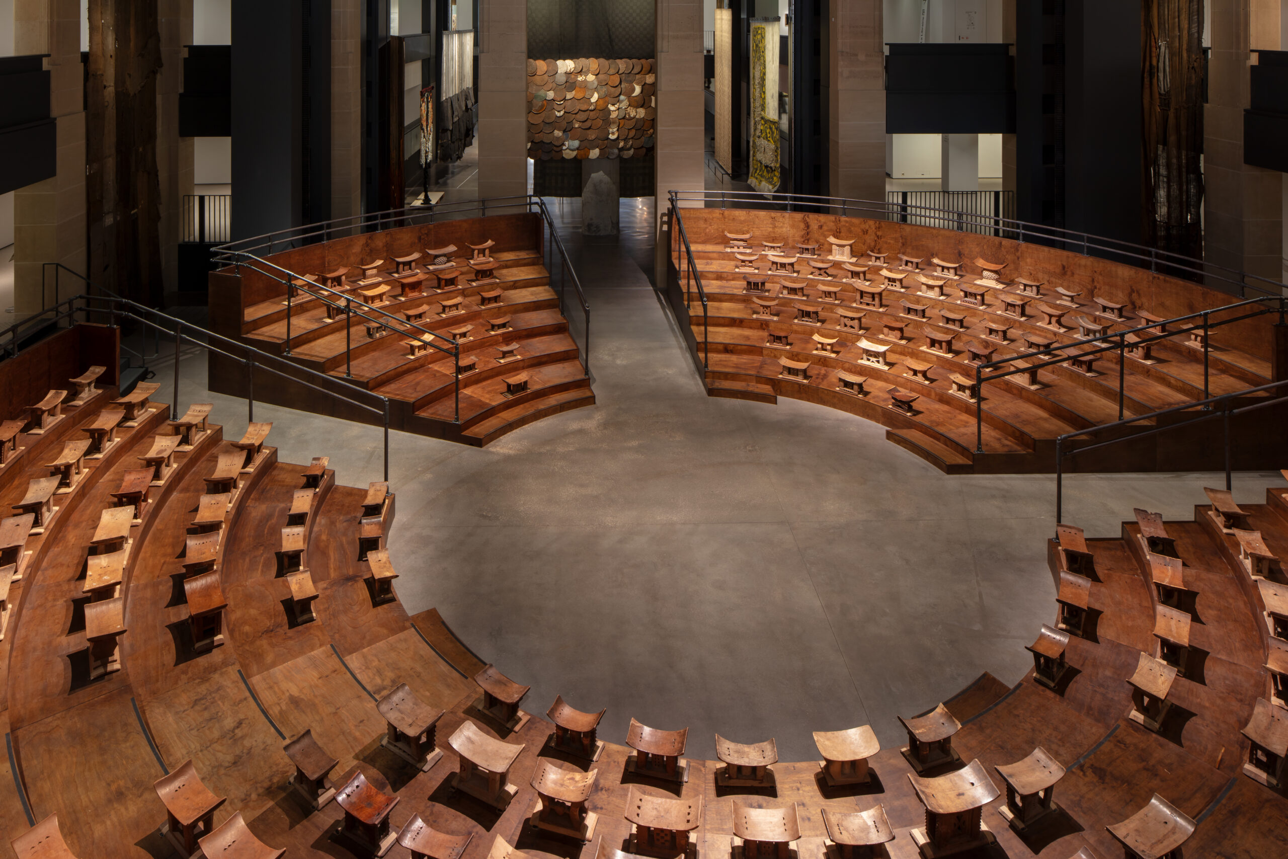 Ibrahim Mahama Brings Ghana's Industrial Past to Paris 2 Wooden Asante stools arranged on curved tiers around an empty central floor in a parliamentary chamber installation.