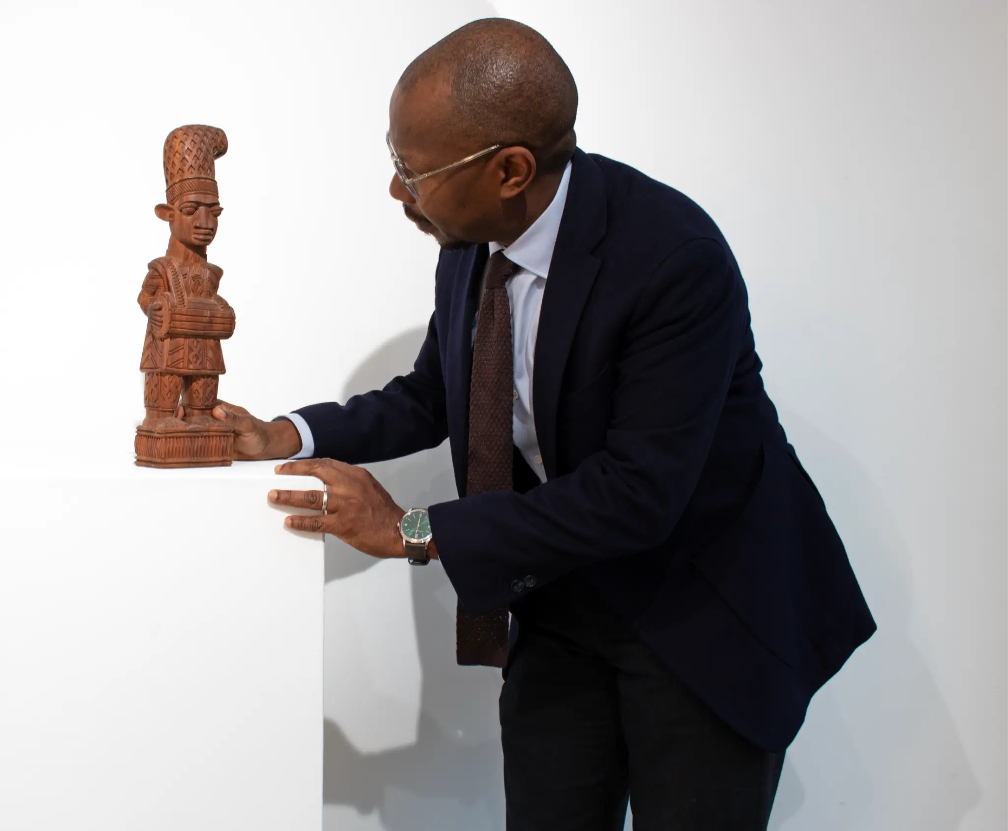 TAFETA founder Ayo Adeyinka examines a carved wooden figure by Lamidi Olonade Fakeye on a white plinth.