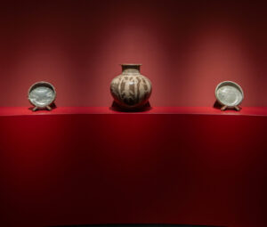 A Ladi Kwali water pot and two plates displayed against a red backdrop at TAFETA’s TEFAF Maastricht presentation.