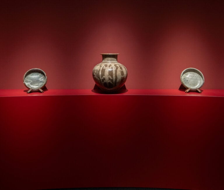 A Ladi Kwali water pot and two plates displayed against a red backdrop at TAFETA’s TEFAF Maastricht presentation.