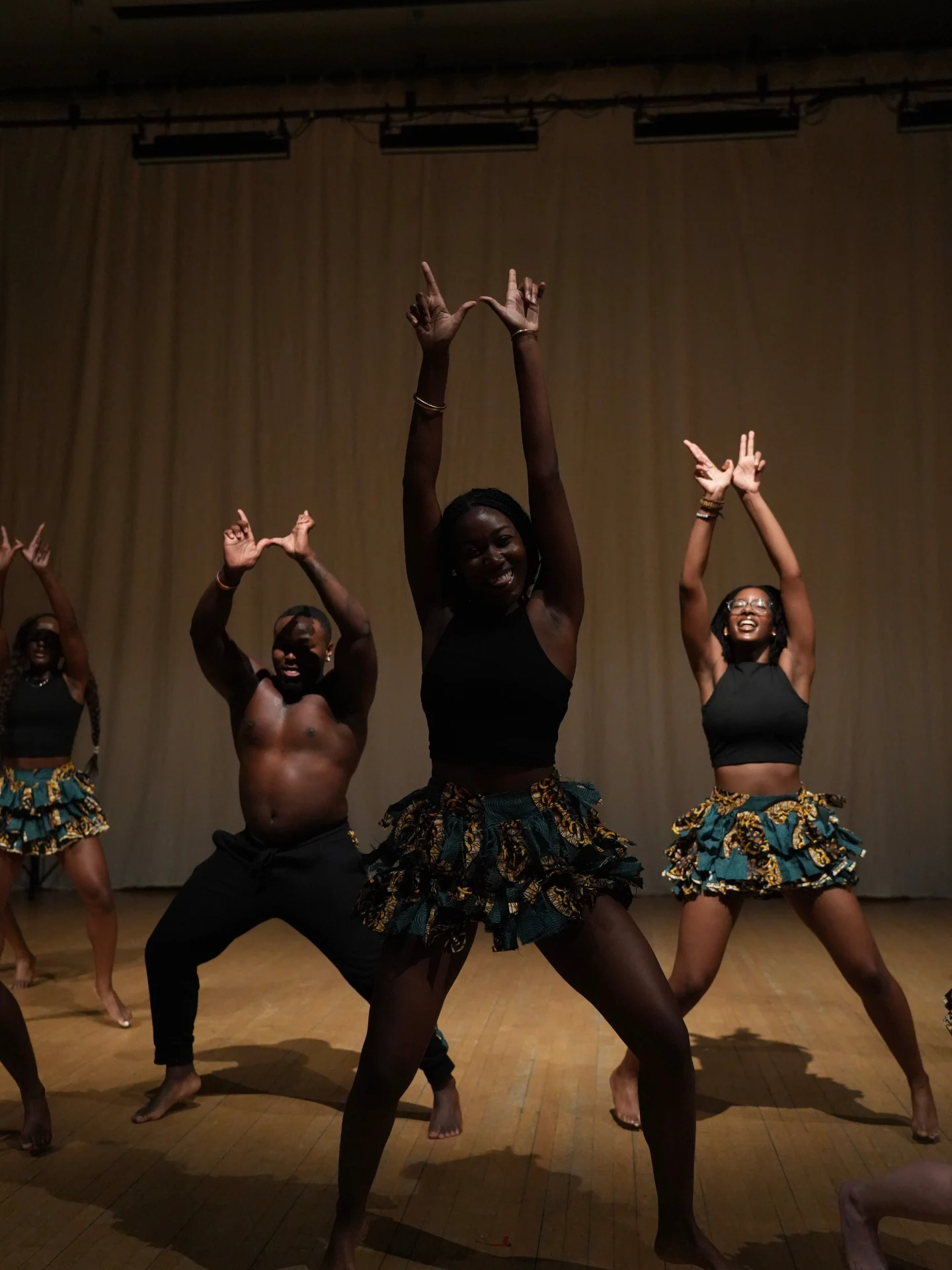 Harvard dancers raise their arms in matching green and yellow skirts.
