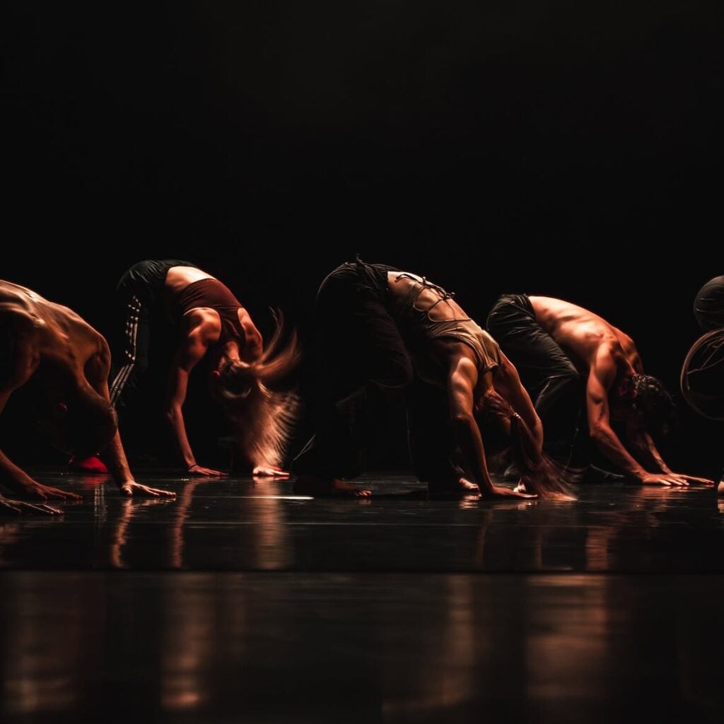 Dancers arch backwards on a dark stage in Dickson Mbi’s TELLUS at Jerwood DanceHouse.
