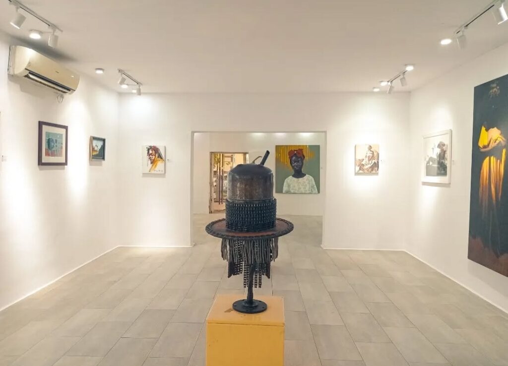 Paintings on white walls and a sculpture on a yellow plinth at Omenka Gallery in Ikoyi, Lagos, during Lagos Gallery Weekend 2024.