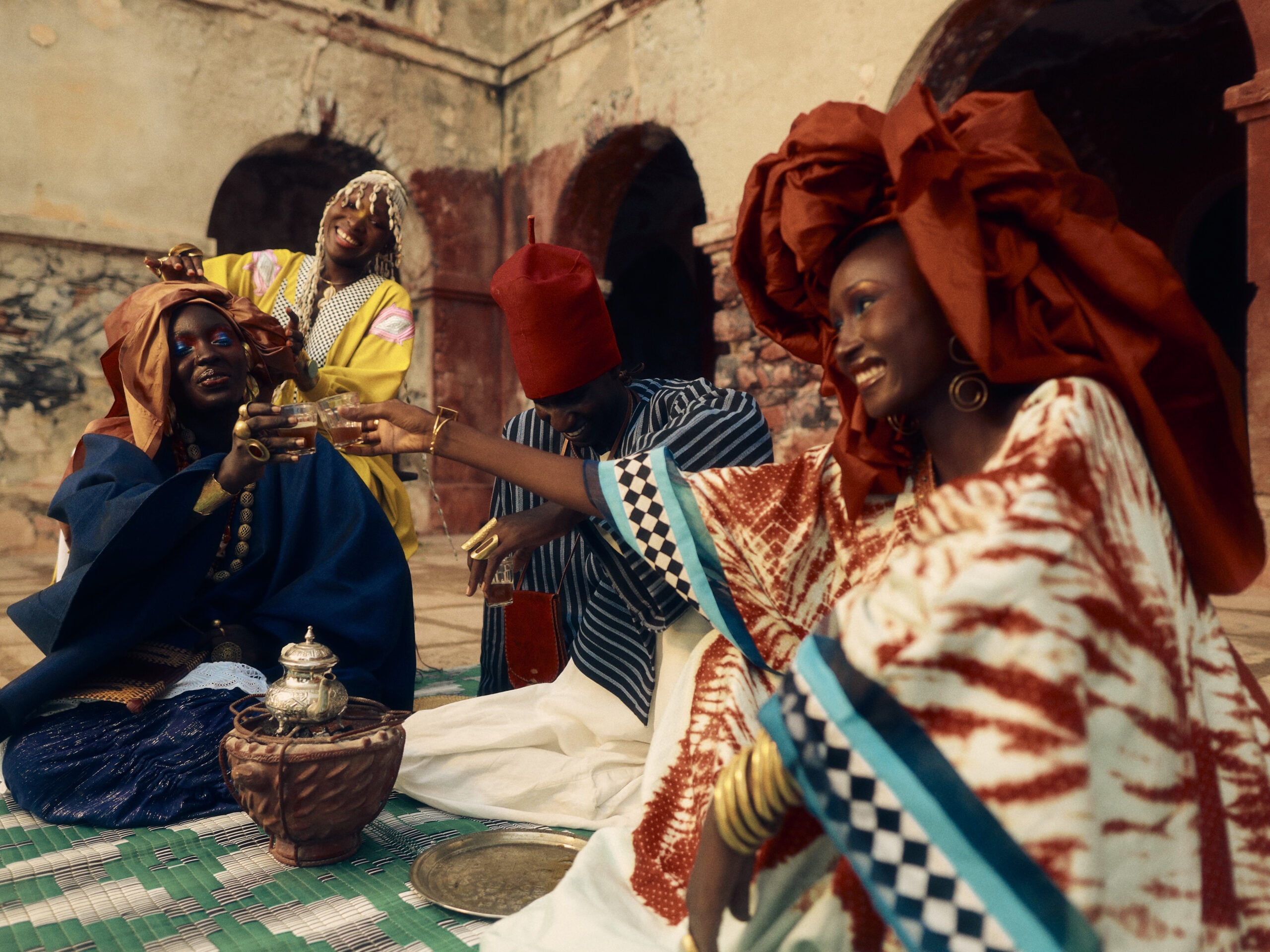 Four people share attaya beside a silver teapot and clay brazier in the courtyard of the Palais du Gouverneur on Gorée, Senegal.