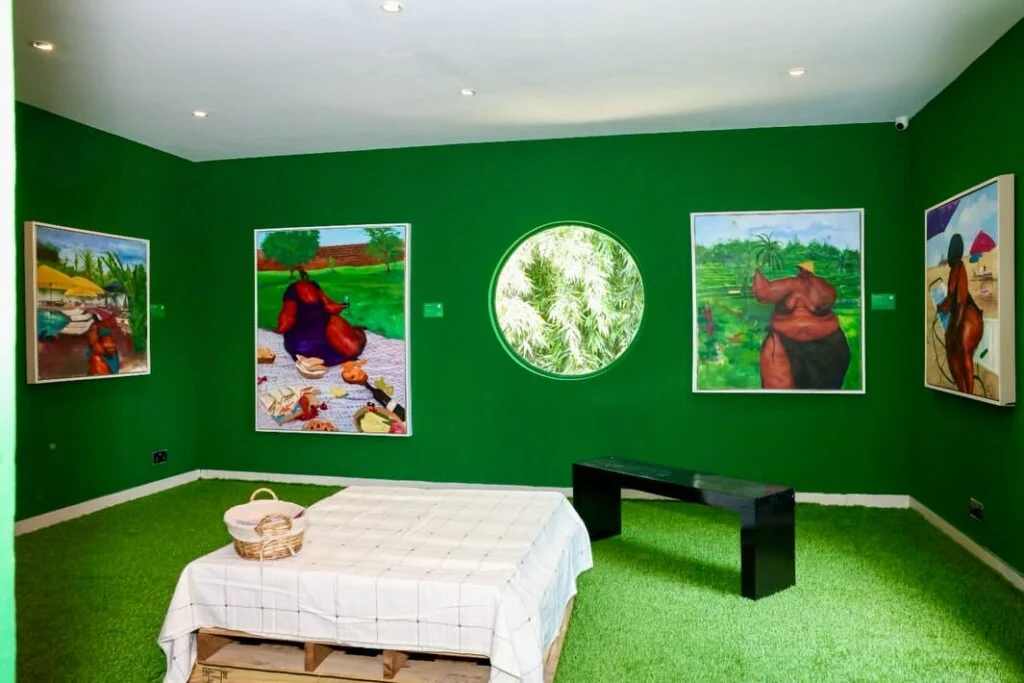 Uthman Wahaab’s paintings surround a picnic setting and circular window in a green-walled room at Windsor Gallery, Lagos.