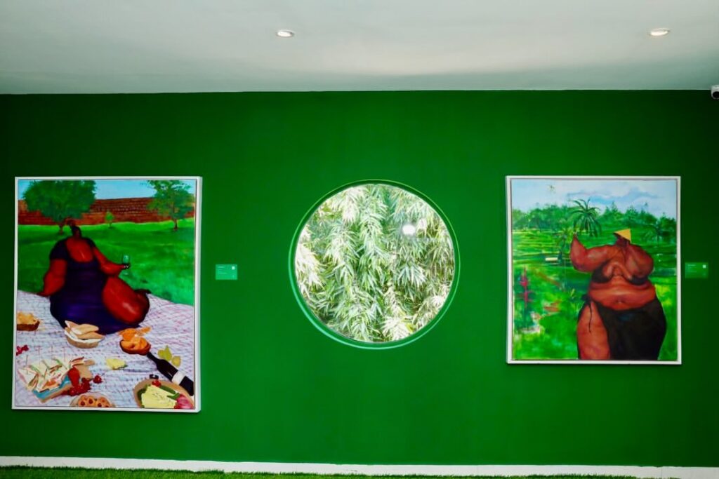 Uthman Wahaab’s paintings surround a picnic setting and circular window in a green-walled room at Windsor Gallery, Lagos.