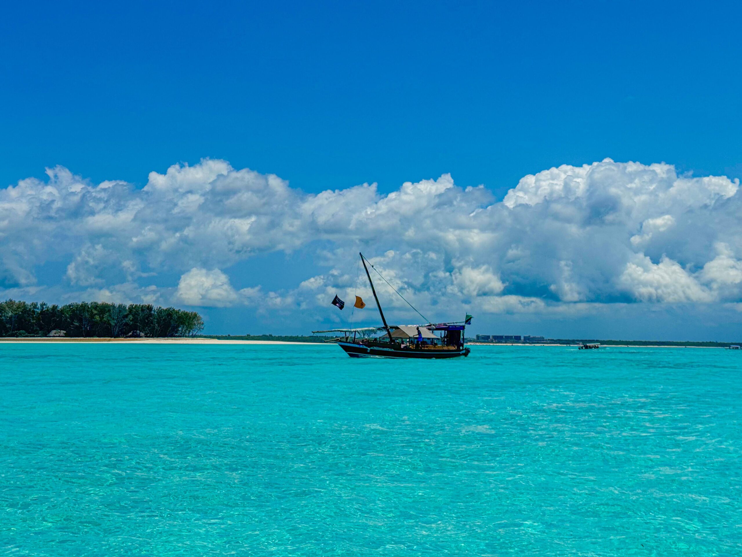 A wooden dhow on turquoise water off Zanzibar beneath a blue sky and white clouds.