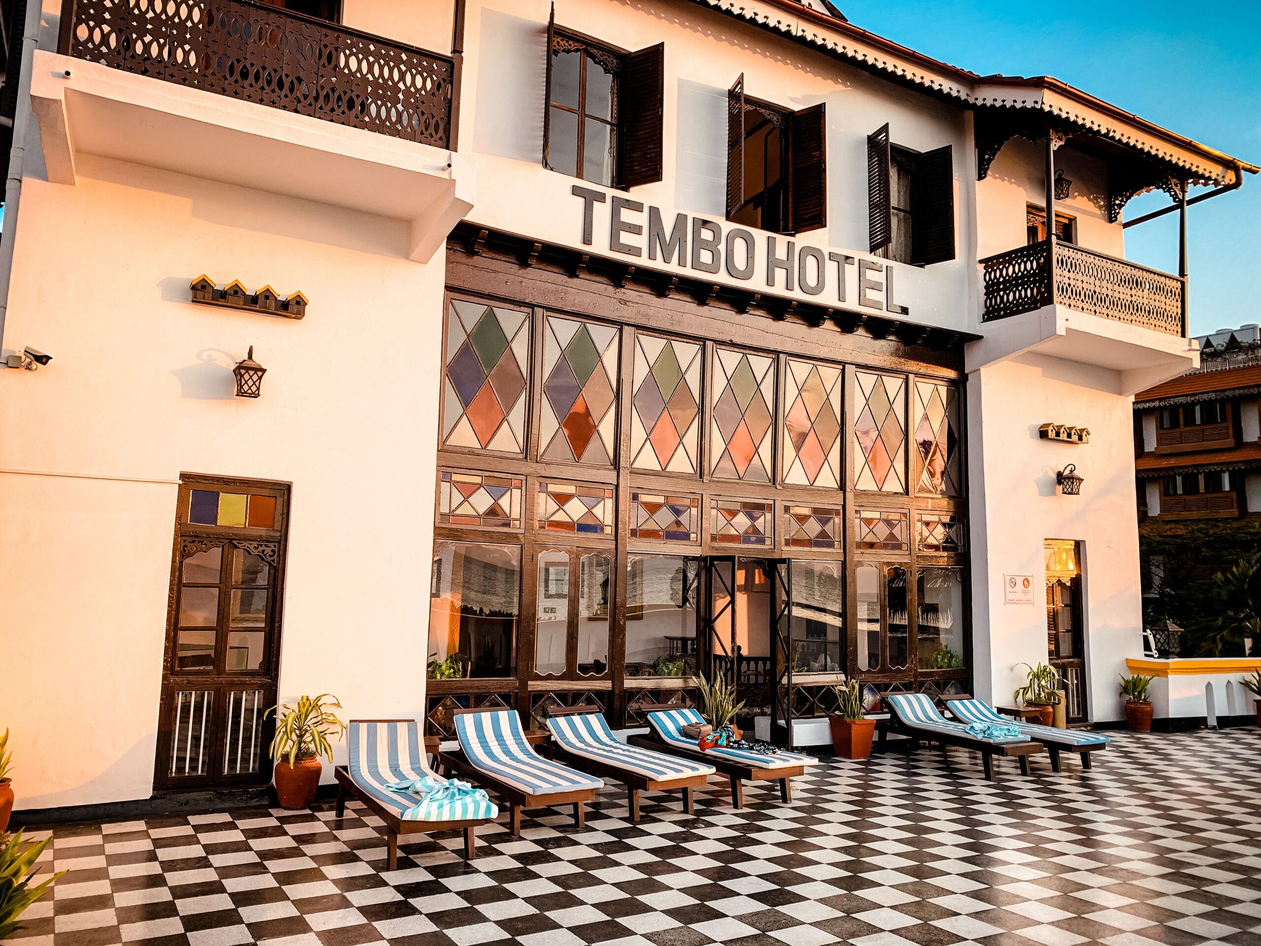 The facade of Tembo Hotel in Zanzibar, with carved wooden doors and lounge chairs on a tiled terrace.