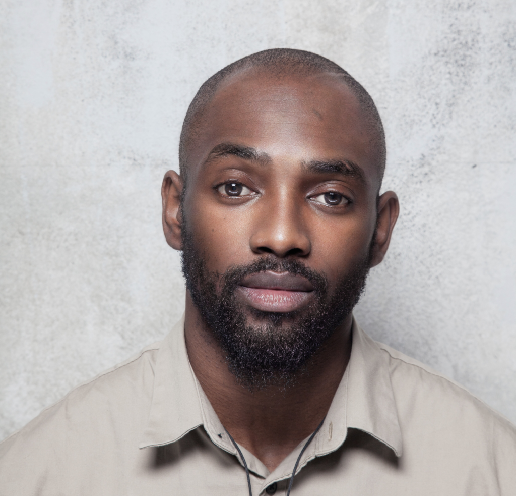 Portrait of choreographer and composer Dickson Mbi in a beige shirt against a pale background.